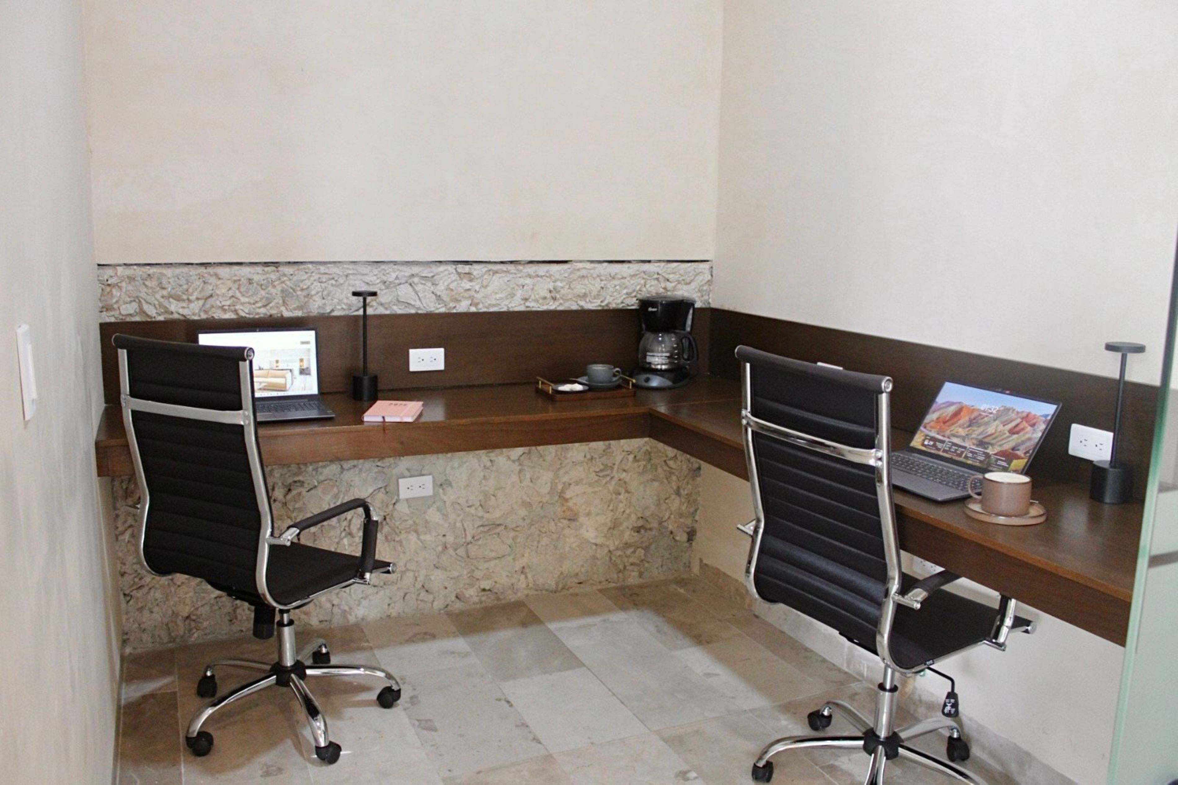 A small office space with two black office chairs, a wooden desk, a laptop, a coffee maker, and a cup.