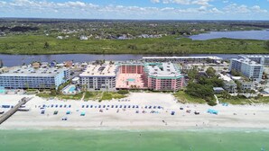 Un hotel frente al mar con varias construcciones, una playa con sombrillas y un puerto deportivo.