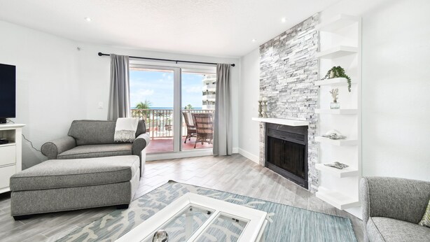 Una sala de estar moderna con chimenea, sofás grises, televisor y un balcón con vistas al mar.
