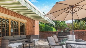 A patio with outdoor furniture, a large umbrella, and a brick wall.