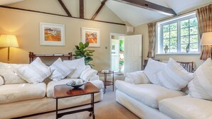 A living room with two white sofas, a wooden coffee table, and a door leading to a garden.
