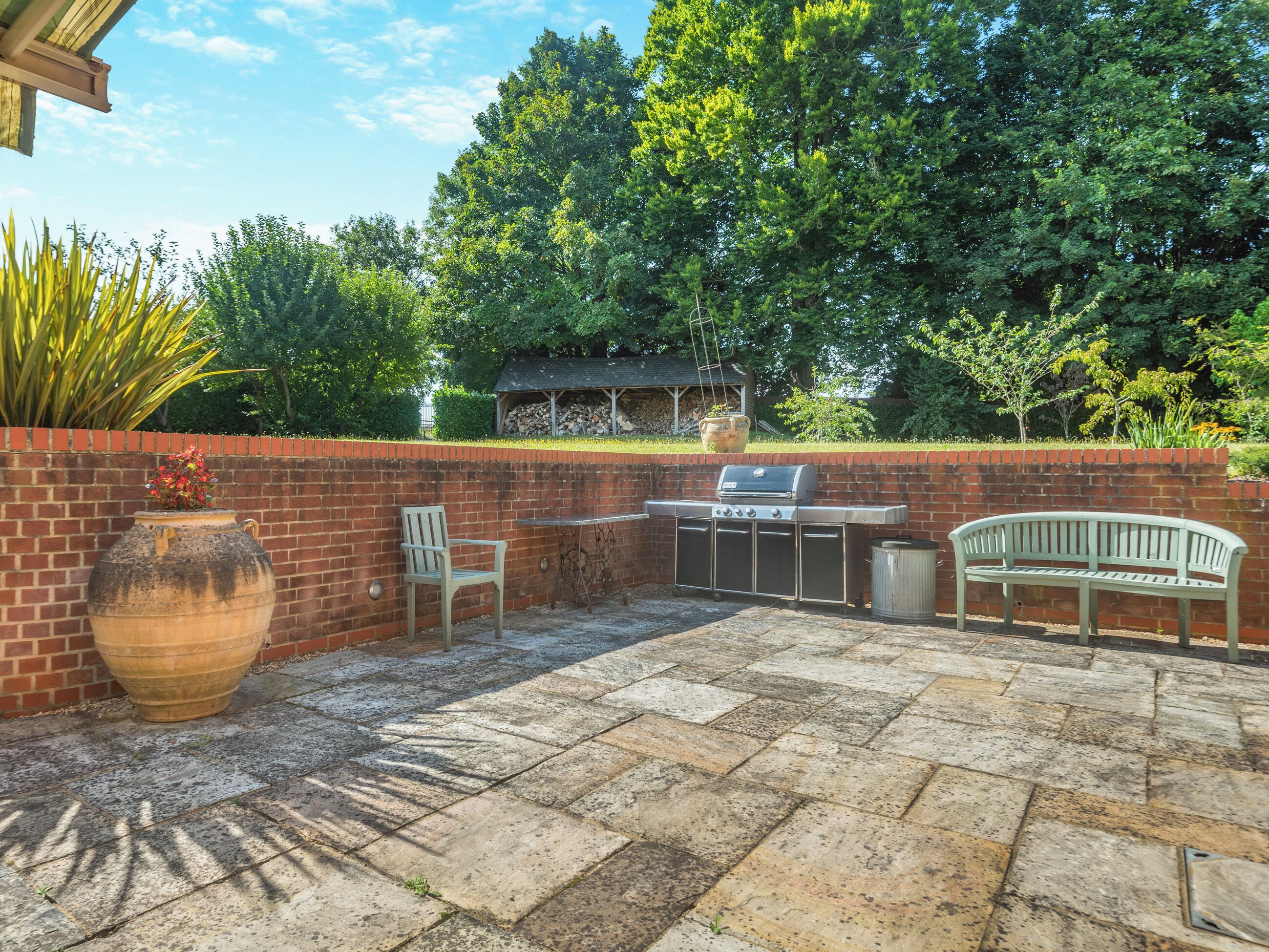 An outdoor patio with a grill, seating, and a brick wall.