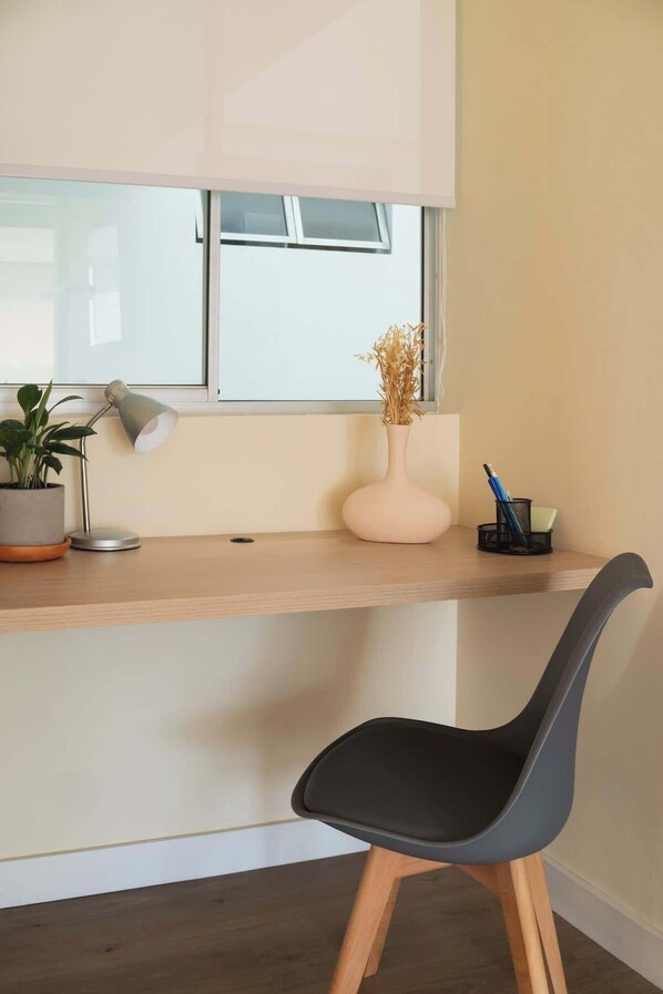 A modern workspace with a wooden desk, a black chair, a potted plant, a desk lamp, a vase with dried flowers, and a pen holder. - Private Terrace Duplex in El Poblado (Medellin)