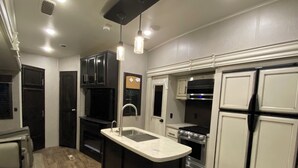 Uma cozinha compacta com ilha central, eletrodomésticos embutidos e iluminação pendente.