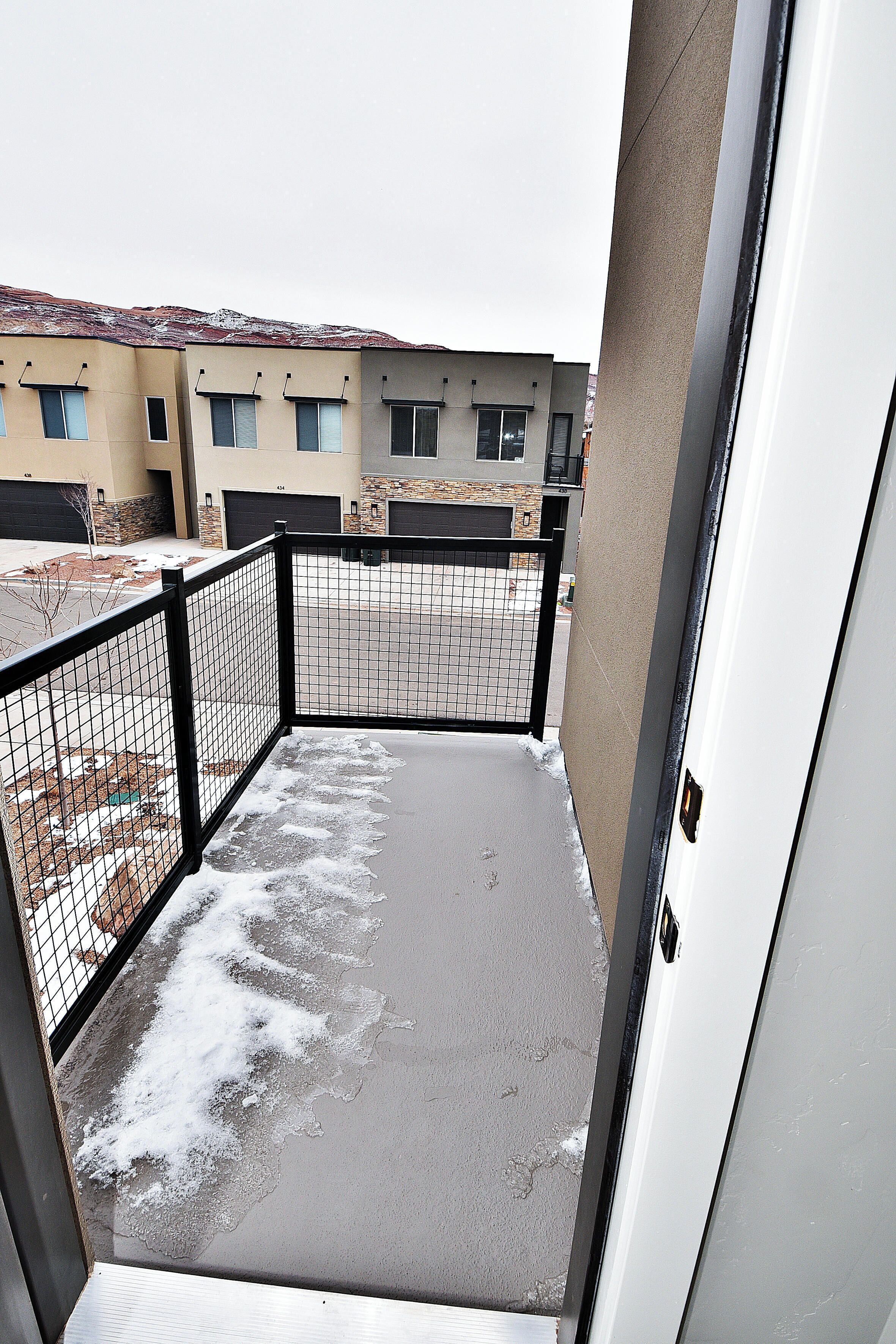 A balcony with a metal fence, a concrete floor, and a view of buildings in the background.