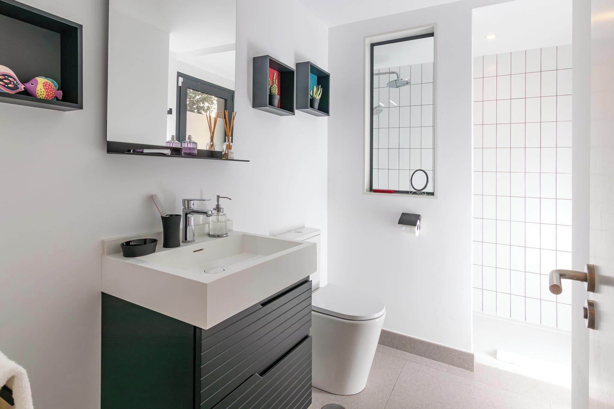 A modern bathroom with a white sink, dark cabinetry, a toilet, and a shower with a grid-patterned glass door.