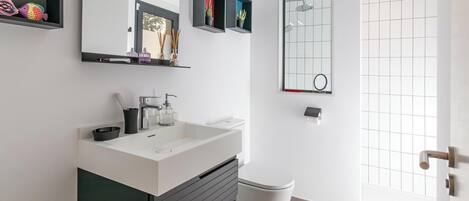 A modern bathroom with a white sink, dark cabinetry, a toilet, and a shower with a grid-patterned glass door.