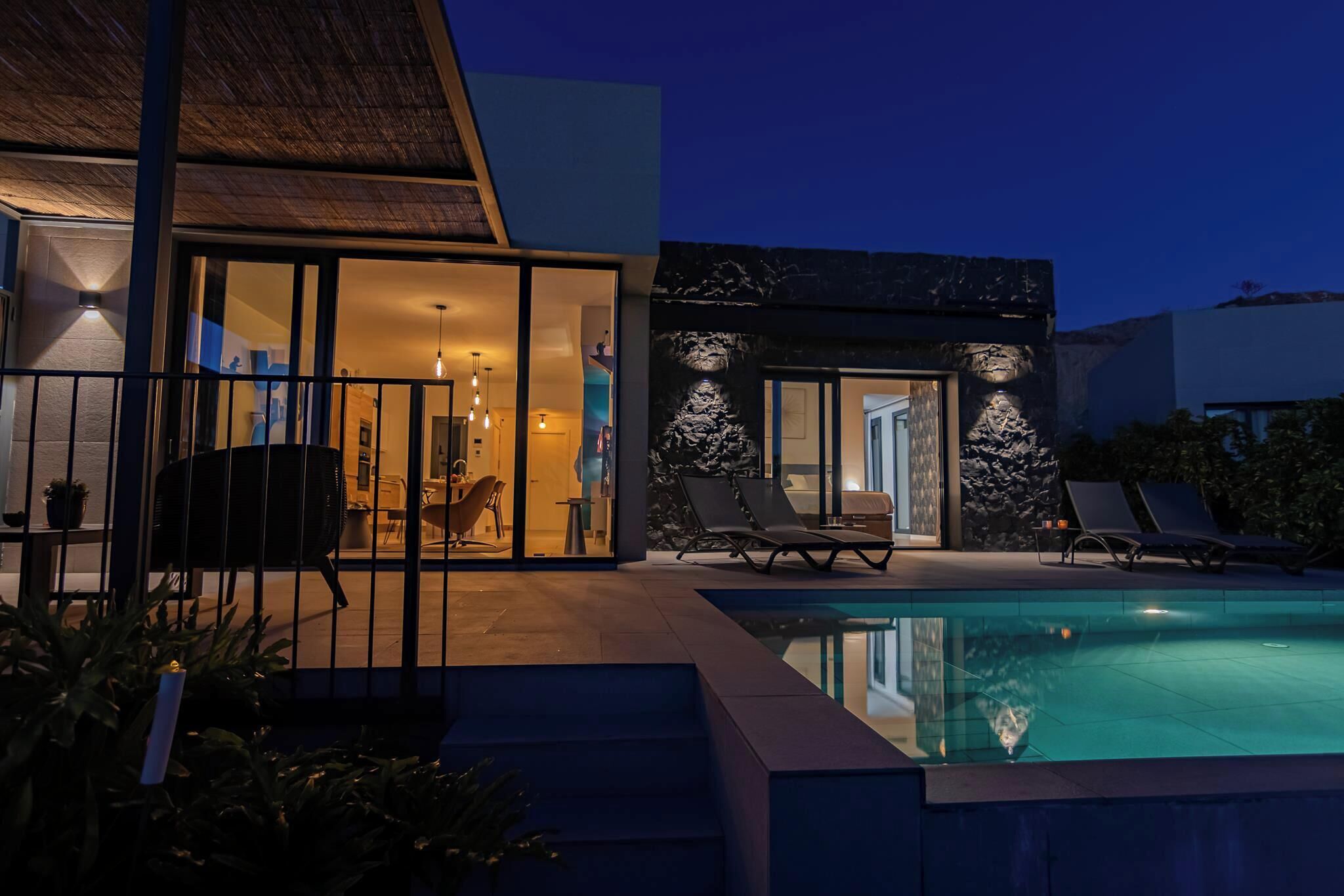 Une maison moderne dotée d’une piscine, de portes vitrées et d’un espace salon extérieur.