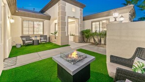 Une maison moderne dotée d’un patio comprenant un foyer extérieur, du mobilier de jardin et une pelouse bien entretenue.