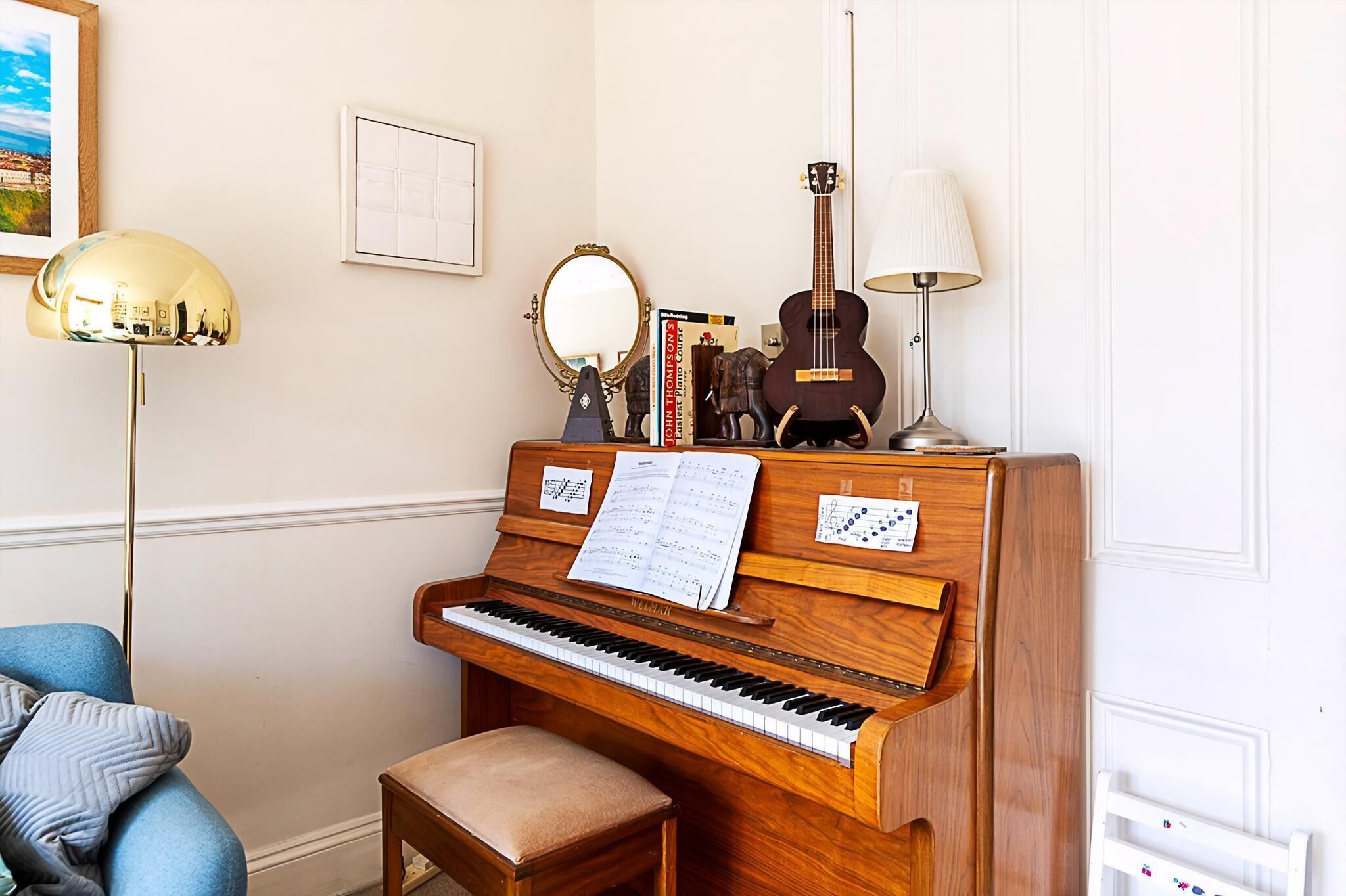 A piano with sheet music, a mirror, and a guitar on a wooden stand.