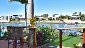Un área junto a la piscina con sillas de mimbre, una palmera y vista a un lago con casas al fondo.