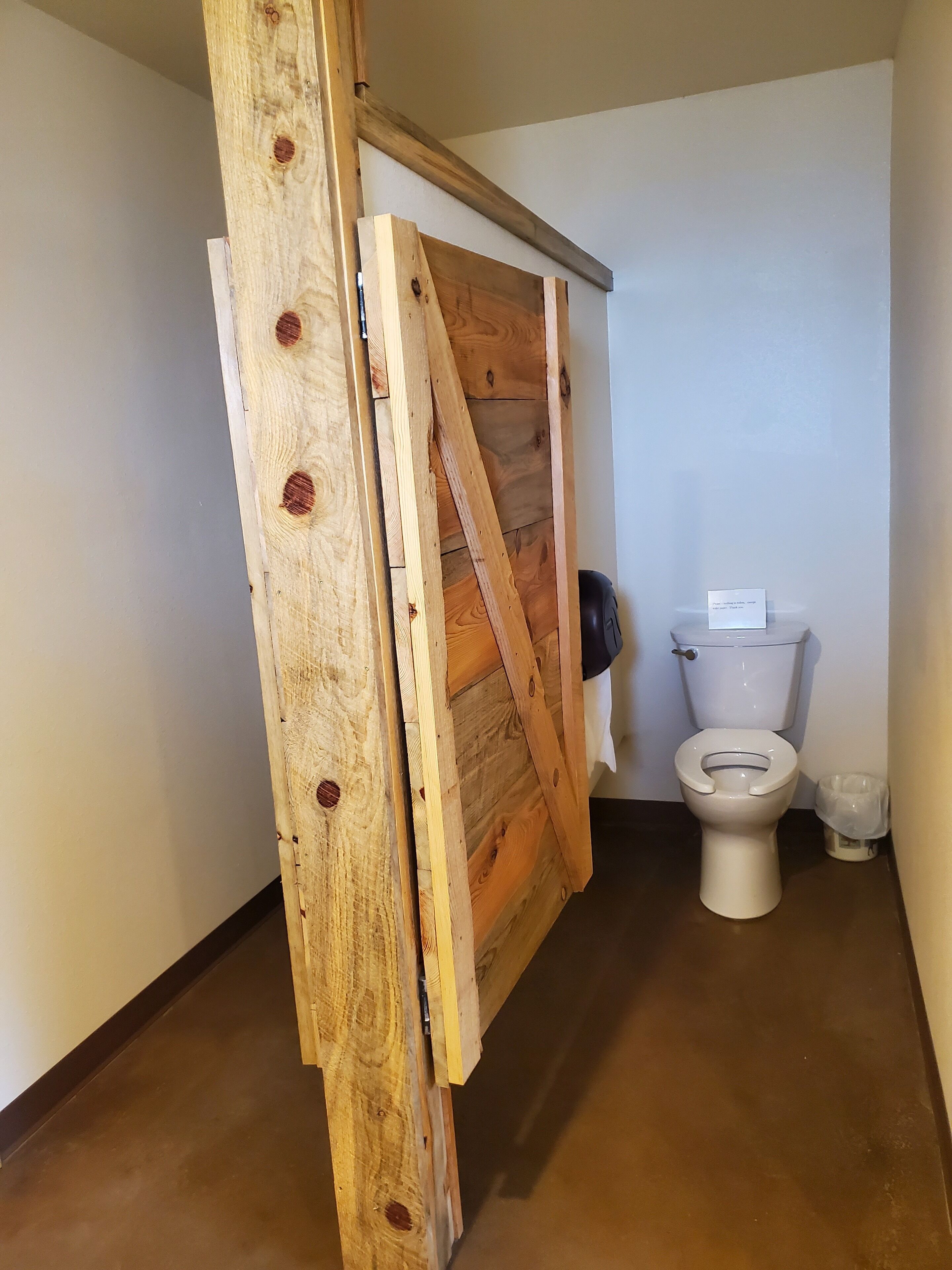A bathroom with a wooden door, a toilet, and a trash bin.