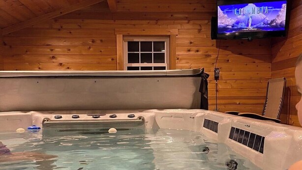L’intérieur d’un chalet en bois, avec un jacuzzi, un téléviseur fixé au mur et une fenêtre.