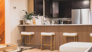 A modern kitchen with dark wooden cabinets, a stainless steel refrigerator, and a built-in island with stools.
