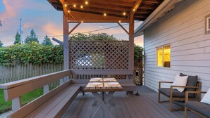 An outdoor deck with a wooden table and benches, surrounded by a wooden fence and a house.