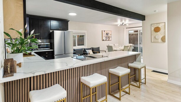 A modern kitchen with a central island, black cabinets, stainless steel appliances, and a seating area with bar stools.