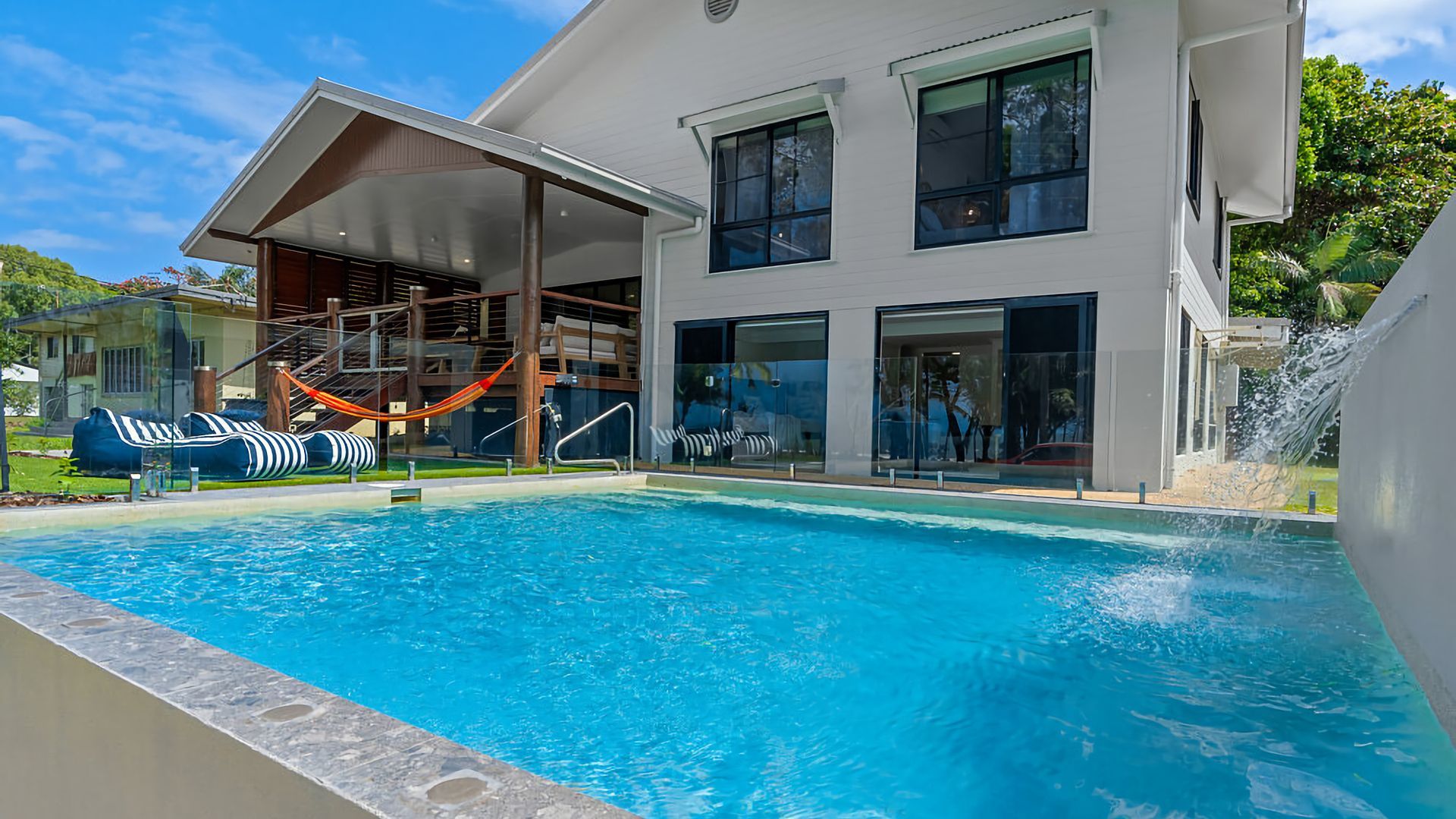 Una casa moderna con piscina, un'amaca e un elemento d'acqua.