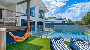Una casa moderna con piscina, hamaca y sillas de descanso.