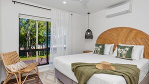 Un dormitorio con una cama grande, vistas al exterior, una silla de mimbre y un ventilador de techo.