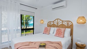 Un dormitorio con cama, ventana con vista a la playa, aire acondicionado de pared y lámpara de noche.