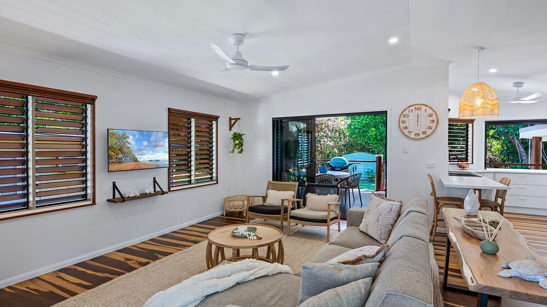 A modern living room with a sofa, chairs, a dining table, and a ceiling fan.