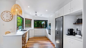 A modern kitchen with a central island, stainless steel appliances, and a view of greenery outside.