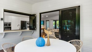 Una cocina moderna con armarios blancos, un espejo con marco negro y una zona de comedor con una mesa redonda y sillas de mimbre.