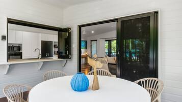 A modern kitchen with white cabinetry, a black-framed mirror, and a dining area with a round table and wicker chairs.