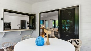 Une cuisine moderne avec des meubles blancs, un miroir à cadre noir et un coin repas comprenant une table ronde et des chaises en osier.