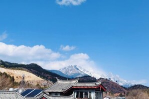 A traditional building with a red roof and white walls, set against a mountainous backdrop with snow-capped peaks. - Lijiang Blue Stone Inn (Lijiang)