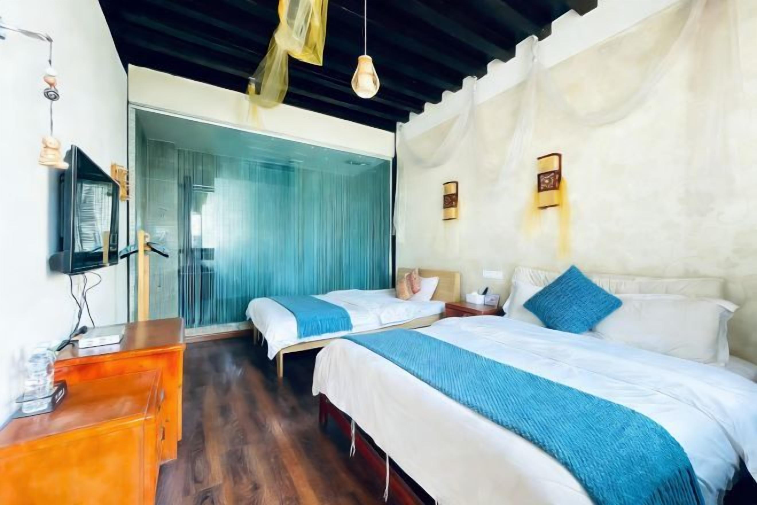 Habitación de hotel con dos camas, un aparador de madera, un televisor y un ventanal corredero que da a un balcón.