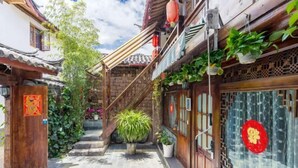 Ein traditioneller Innenhof mit Steintreppe, Holztür mit roter Verzierung und Blumentöpfen.