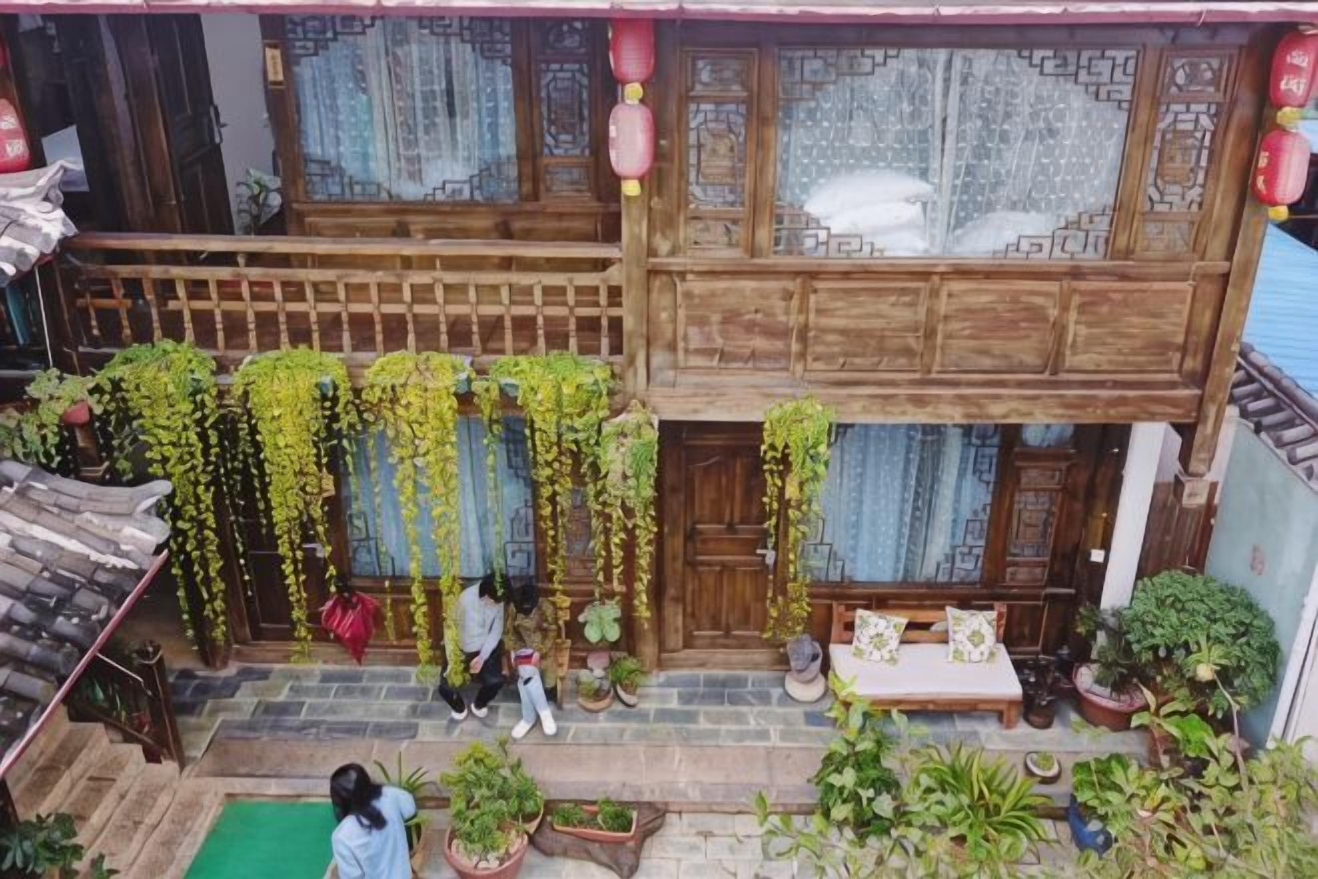 Un edificio tradicional de madera con un balcón, macetas con plantas y un pequeño espacio para sentarse.