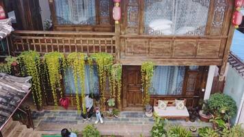 Un edificio tradicional de madera con un balcón, macetas con plantas y un pequeño espacio para sentarse.