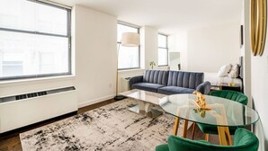 A modern living room with a glass coffee table, a sofa, and a dining area with green chairs. - Beautiful Studio Downtown NYC (New York)