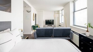 A modern bedroom with a bed, a sofa, a TV, a lamp, and a window. - Beautiful Studio Downtown NYC (New York)