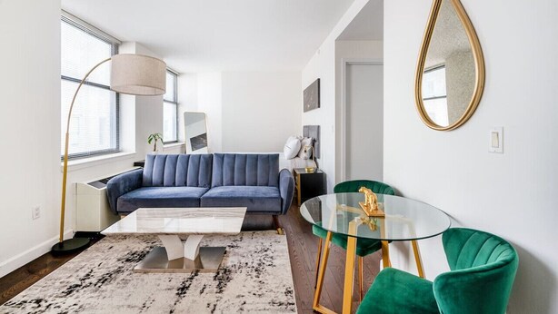 A modern living room with a blue sofa, a glass coffee table, and green chairs. - Beautiful Studio Downtown NYC (New York)
