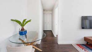 A modern interior with a glass table, a potted plant, a TV, and a wooden bench. - 2 Bedroom Gem in Financial (New York)