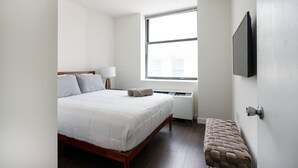 A bedroom with a bed, a window, a wall-mounted TV, and a bench. - 2 Bedroom Gem in Financial (New York)