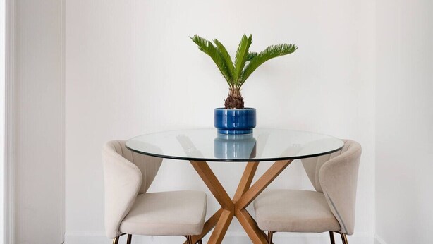 A round glass table with a blue pot and a plant, flanked by two beige chairs with wooden legs. - 2 Bedroom Gem in Financial (New York)