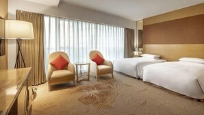 Une chambre d’hôtel avec deux lits, un bureau, une chaise, une lampe et une grande fenêtre avec des rideaux.