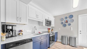 A modern kitchen with white and blue cabinets, stainless steel appliances, and a herringbone tile backsplash.