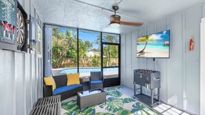 A sunlit room with a pool view, a ceiling fan, a foosball table, and a dartboard.