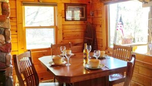 Une table de salle à manger en bois, mise avec des assiettes, des bols et des verres à vin, entourée de chaises en bois.