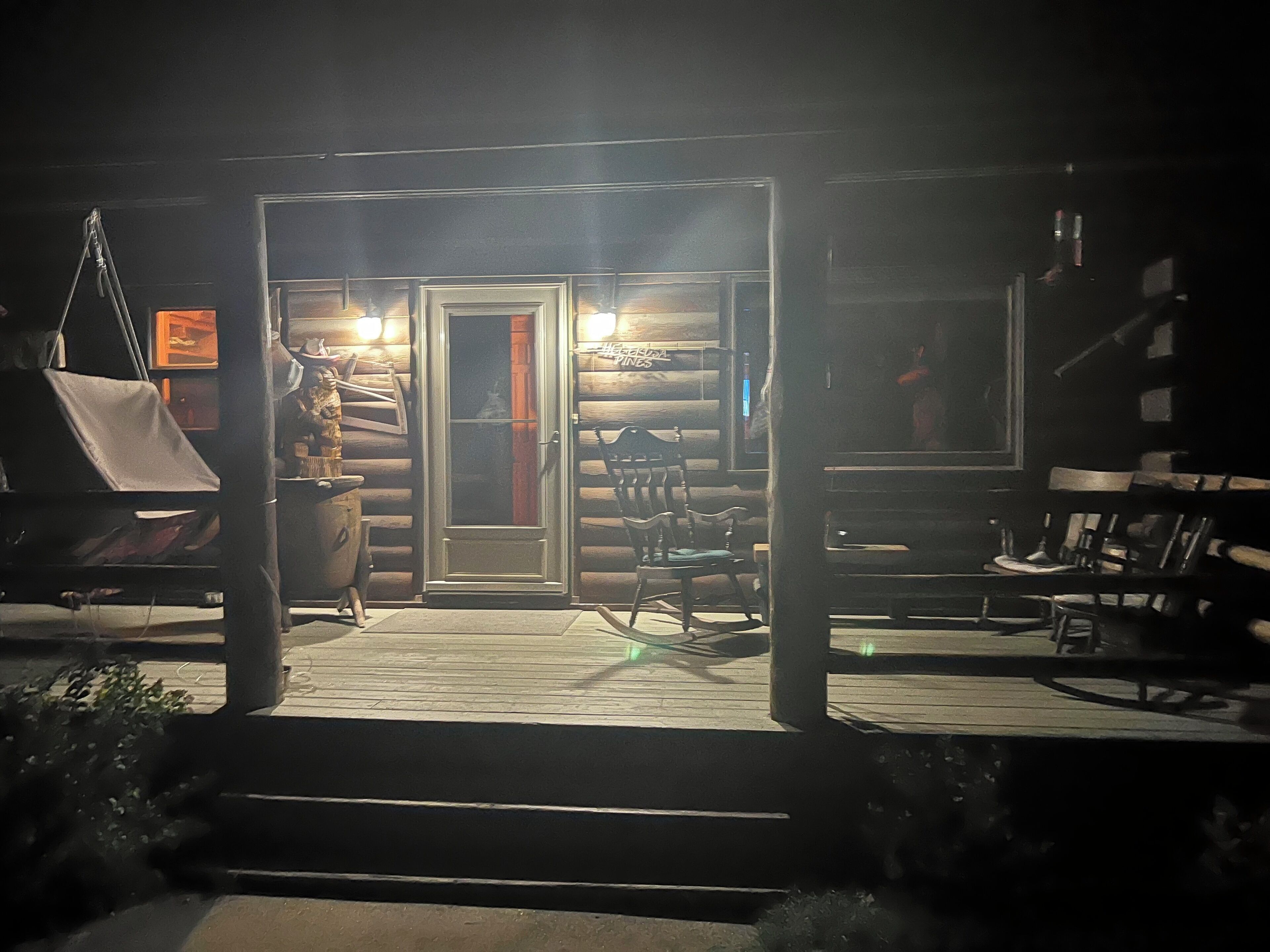 A wooden cabin with a porch, a grill, and a chair.