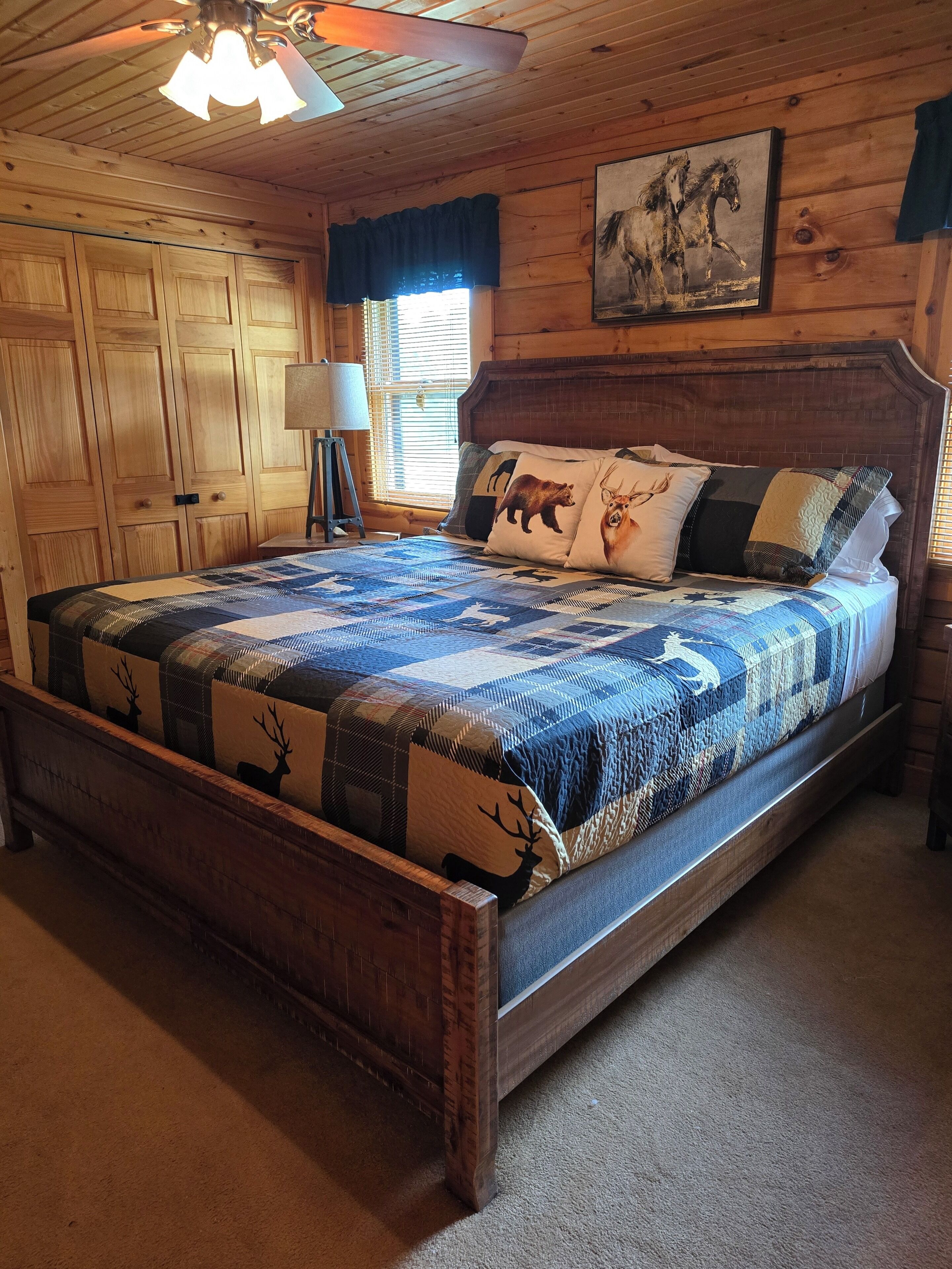 Un dormitorio con paneles de madera, una cama grande, un ventilador de techo y un cuadro de caballos.