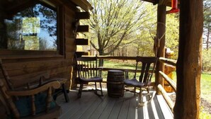 Une terrasse en bois avec une pièce de style rustique évoquant un chalet, comprenant un banc en bois, un fauteuil à bascule et un tonneau.