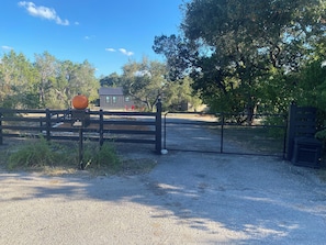 Un camino de grava que conduce a una zona vallada con cerca metálica y puerta de madera.