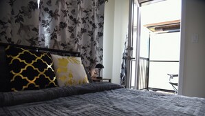 Un dormitorio con cama, cortinas florales y vistas al exterior.