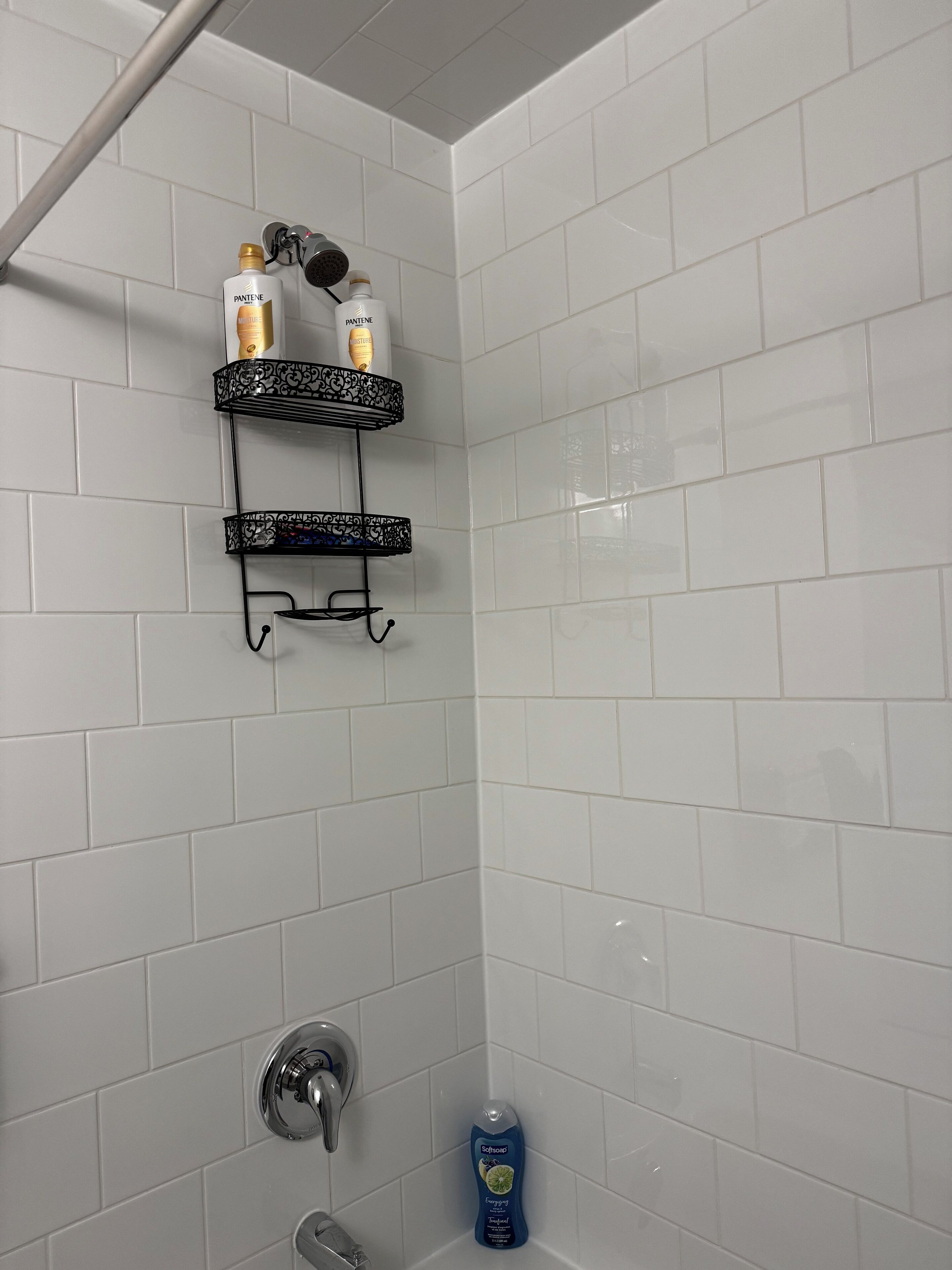 Een badkamer met witte betegelde muren, een douche en twee zwarte planken met toiletartikelen.